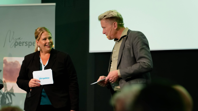 två personer står på en scen och pratar inför publik