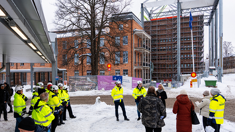 Vy över personer samlade utanför en hög byggnad, många med byggarbetskläder på.
