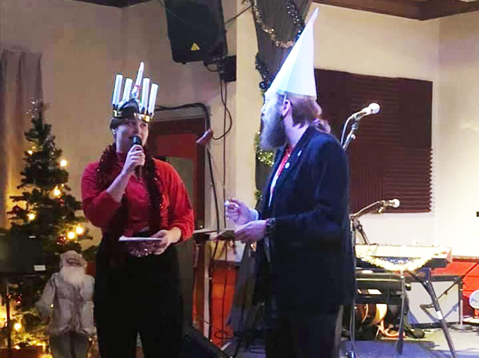 Två personer med luciakrona och tomtemössa sjunger i en kyrka