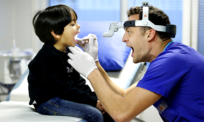 Vårdpersonal undersöker barn i munnen, båda gapar.
