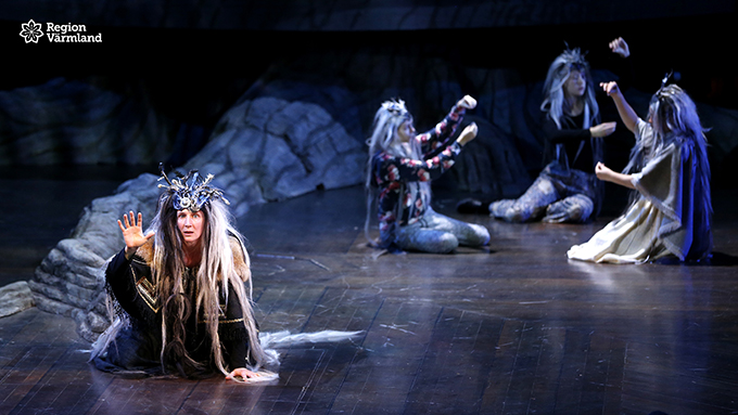 Fyra kostymklädda skådespelare på teaterscen.