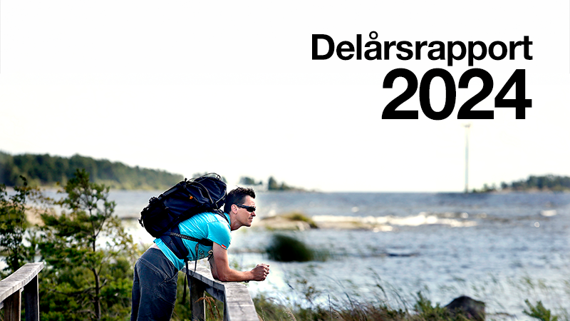 En man med ryggsäck står lutad över ett trästaket och blickar ut. I bakgrunden syns en större sjö. Över bilden ligger texten Delårsrapport 2024.