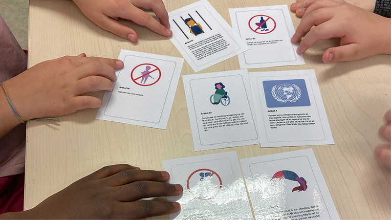 På bilden syns flera barnhänder tillsammans med en kortlek med några uppvända kort.