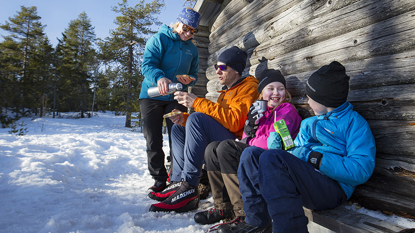Familj fikar i vid vindskydd i vinterlandskap.