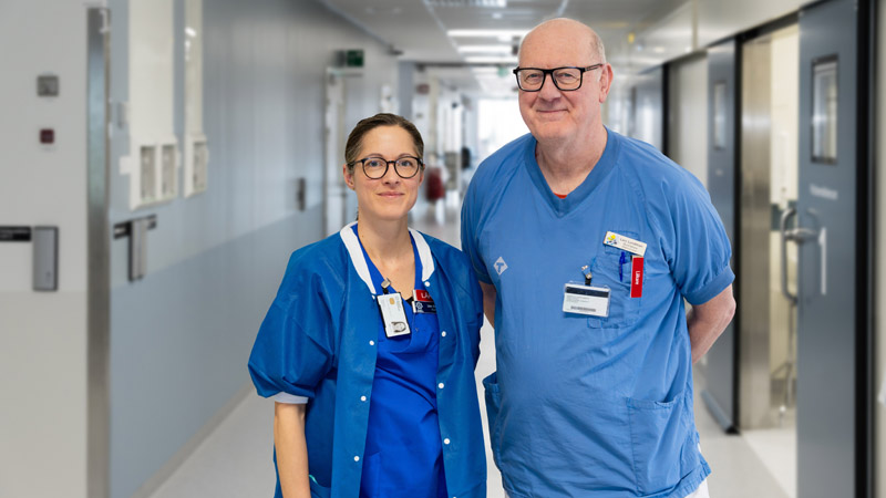 Två läkare i hälso- och sjukvårdens blåvita kläder. Bilden är tagen i en sjukhuskorridor.