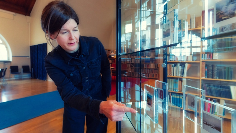 En person står vid en glasmonter som innehåller polaroidbilder. Personen pekar på en av bilderna.