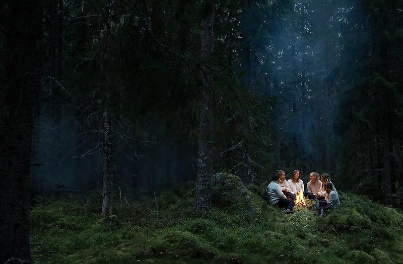 Människor runt en eld i en mörk och mystisk granskog