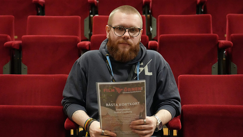 Vinnaren sitter och håller upp sitt vinstintyg i en biosalong.