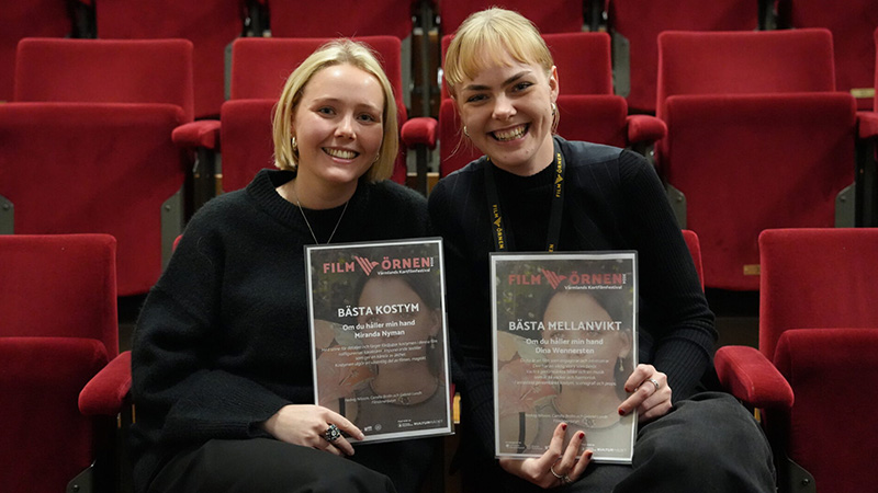Två personer håller upp sina vinstintyg sittandes i en biosalong.