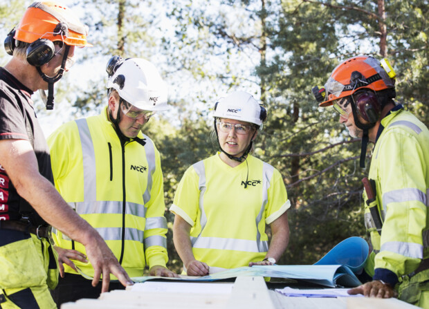 Fyra byggarbetare som samtalar över en ritning.