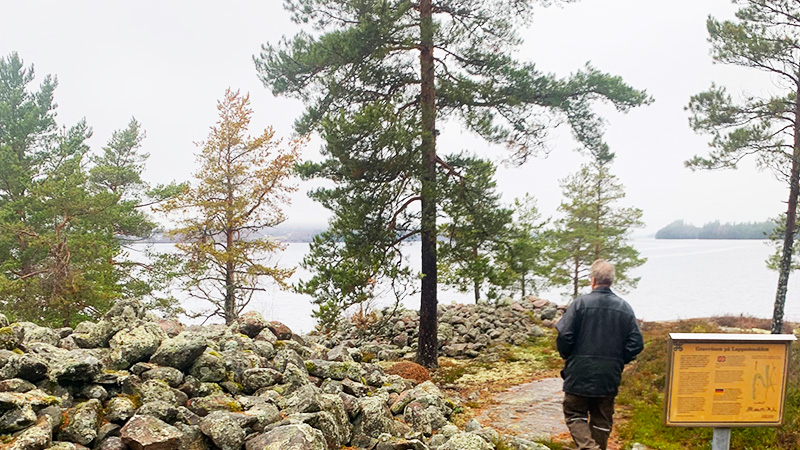 En person går förbi ett stenröse mot sjön Fryken. 