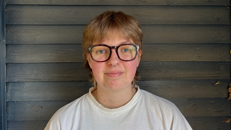 Person i kort hår, glasögon och vit t-shirt.