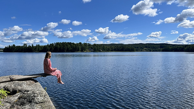 Sommarbild där en person sitter på klippa vid vatten