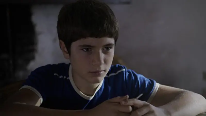 En pojke sitter lutad över ett bord.