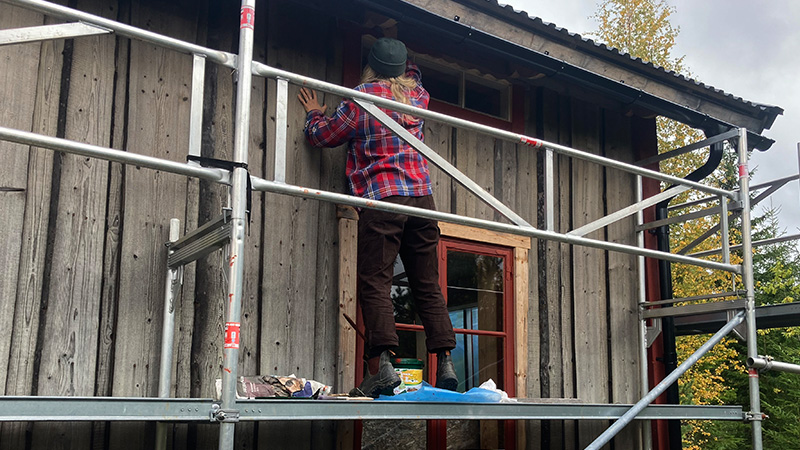 Person som står på en byggnadsställning och snickrar på ett hus
