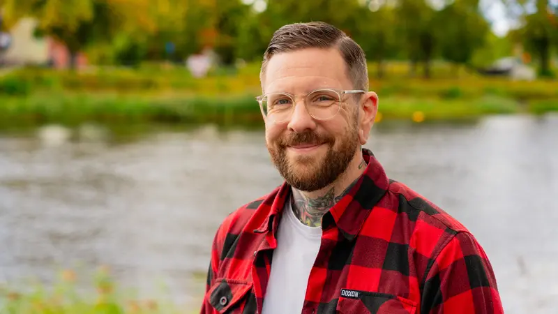 Leende välkammad man med glasögon och tatueringar.