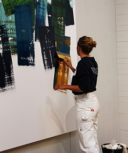 Kursläraren Hertha Hansson står och målar på en stor canvas. 