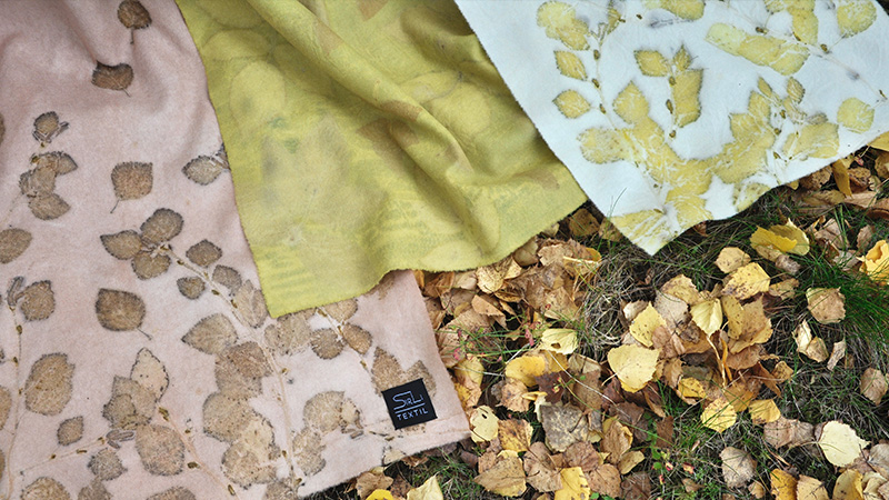Tre tyger med tryck av löv ligger på en lövklädd backe. 