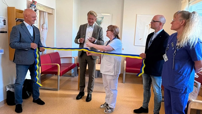Invigning. Fem personer där två klipper ett blågult band.