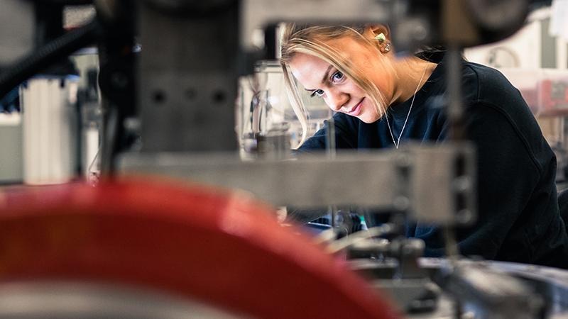En ung kvinna som står vid ett svetsbord och jobbar.