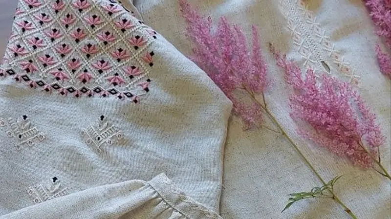Broderad skjorta med traditionella ukrainska mönster i rosa och svart på beige tyg. En kvist av ljung ligger intill broderiet.