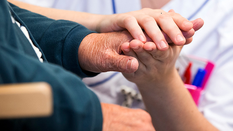 Läkare sitter på huk och håller patientens, som sitter ner, händer i sina.