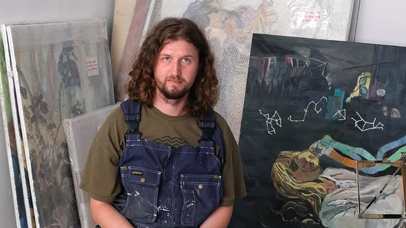 Foto på Jonatan Pihlgren som sitter i arbetskläder framför en tavla.