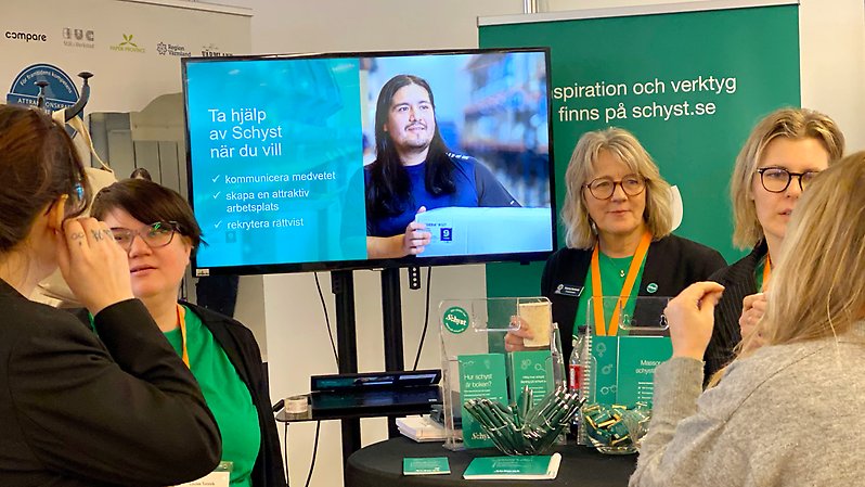 Fem kvinnor står och pratar i en monter.