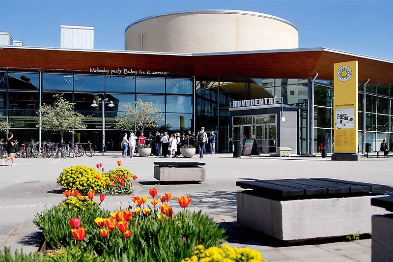 Huvudentrén till Karlstads universitet med blommor i förgrunden.