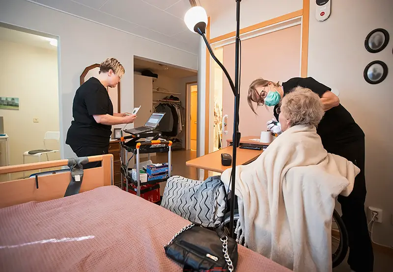 Mimmi skriver på datorn medan Tina undersöker patienten på sitt rum