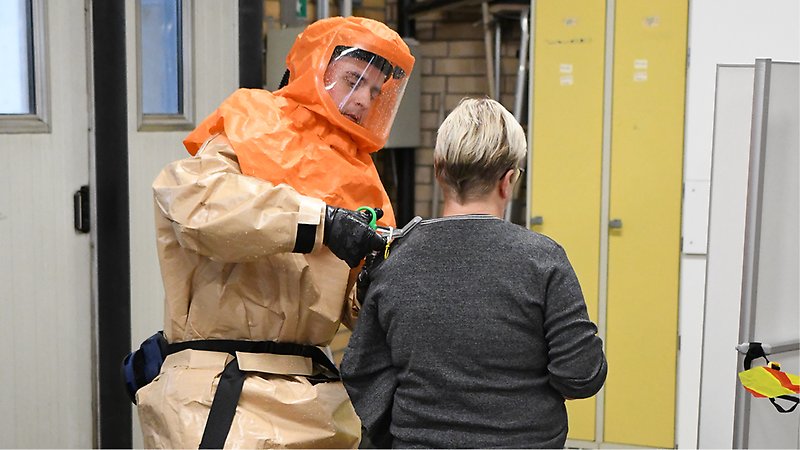 Sjukvårdspersonal i kemdräkt klipper av patients tröja.