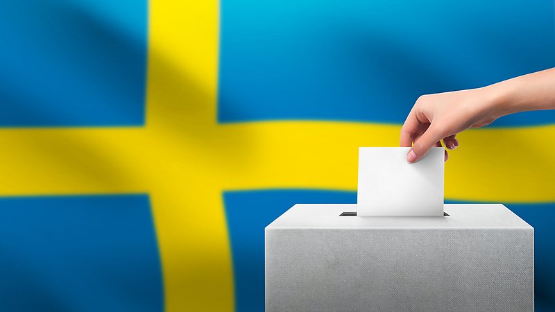 En hand stoppar en röstsedel i en låda. Svenska flaggan i bakgrunden.